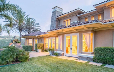 Nice hill top home with a large backyard with a green lawn, shrubs, and tropical trees.